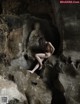 A naked woman sitting on a rock in a cave.