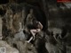 A naked woman sitting on a rock in a cave.