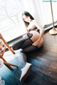 A woman sitting on the floor in black stockings and white shoes.