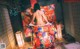 A woman in a colorful kimono sitting on a bed.