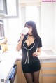 A woman in a black dress drinking from a white cup.