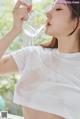 A woman drinking water from a glass in front of a window.