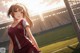 A girl in a red and white uniform standing in front of a soccer field.