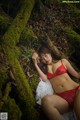 A woman in a red lingerie laying on a moss covered log.