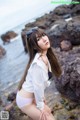 A woman in a white shirt and pink panties posing on a rocky beach.