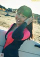 A woman in a wet suit standing next to a surfboard.