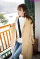 a woman wearing a beige coat and jeans standing on a balcony