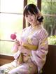 A woman in a pink kimono sitting on a window sill holding a flower.