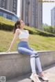 A woman sitting on a concrete wall in a white top and blue leggings.