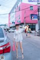 A woman in a white shirt and shorts standing next to a car.