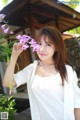 A woman in a white shirt holding a purple flower.