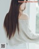 A woman with long brown hair standing by a window.