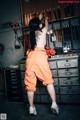 A woman in an orange jumpsuit standing in front of a wall of tools.