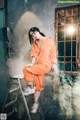 A woman sitting on a ladder in an orange jumpsuit.