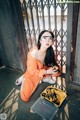 A woman in an orange jumpsuit sitting on the ground next to a yellow tool box.