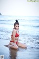 A woman in a red bikini sitting on the beach.