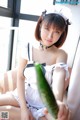 A woman in a maid outfit holding a cucumber.