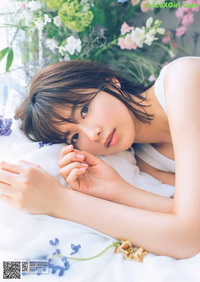 A woman laying on a bed with flowers in the background.