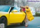 A woman leaning against a yellow sports car in a parking lot.