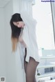 A woman in a white shirt and black pantyhose leaning against a window.