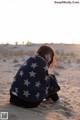 A woman wrapped in a blanket sitting in the sand.