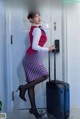 A woman in a red and white uniform is standing next to a blue suitcase.