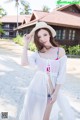 A woman in a white dress and hat posing on a beach.