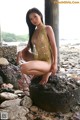 A woman in a yellow bikini sitting on a rock.