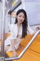 A woman in a white dress sitting on a subway train.