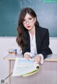 A woman sitting at a desk in front of a blackboard.