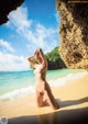 A naked woman sitting on a beach next to the ocean.