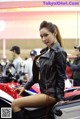 A woman in a leather jacket sitting on a motorcycle.