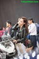 A woman in a leather jacket standing next to a motorcycle.