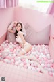 A woman laying on a bed covered in pink and white balloons.